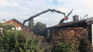Der Kran mit Greifarm der Feuerwehrwehr Hechingen hebt  das Dach des ausgebrannten Wohnhauses ab (links). Das zerstörte Gebäude nach dem Großbrand in Gruol. Im hinteren Teil mussten ebenfalls Nachlöscharbeiten vorgenommen werden.    Foto: Pfeffer