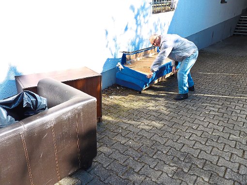 Albert Schnell an der Couch mit gebrochenem Boden. Davor ein schimmeliges Sofa. Foto: Stiller