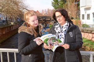 Bettina Reitze-Lotz (rechts) begutachtet mit ihrer Mitarbeiterin Julia Strickfaden das Albtalmagazin 2019 vor dem für die Tourismusregion namensgebenden Albflüsschen Foto: Zoller Foto: Schwarzwälder Bote