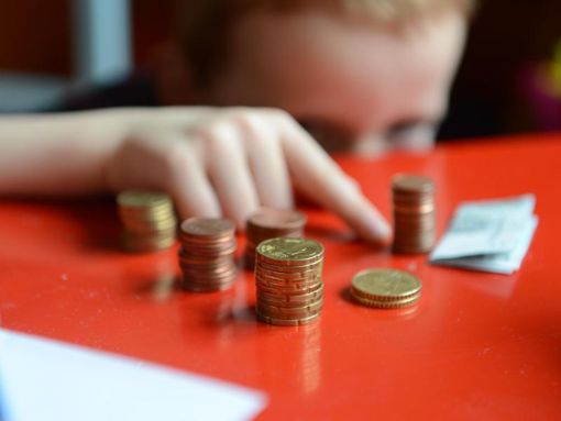 Ein Junge sitzt an einem roten Tisch und zählt Geld. Foto: Jens Kalaene/Archiv/dpa