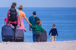 Urlauber und Tagesgäste gehen mit ihrem Reisegepäck an den Strand an der Ostseeküste in Warnemünde. Foto: dpa/Jens Büttner