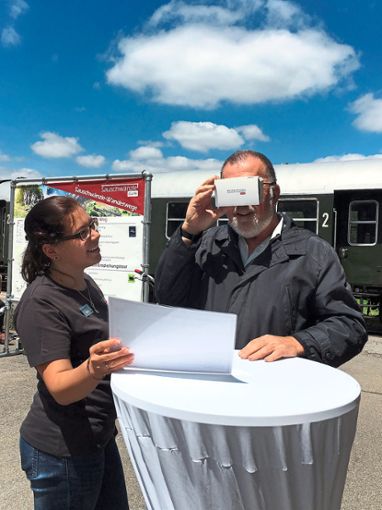 Lorena Bausch von den Bahnbetrieben Blumberg zeigt einem Fahrgast das neue Erlebnis-Angebot mit der Kartonbrille und der virtuellen 360-Grad-Fahrt.  Foto: Löffler Foto: Schwarzwälder Bote
