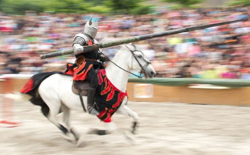 Ein Mann reitet während eines Ritterturniers im Rahmen der 18. Maximilian Ritterspiele in einem Ritterkostüm auf einem Pferd und hält eine Lanze. Foto: dpa