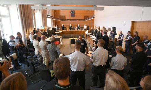 Zu Beginn des Prozesses stehen elf Angeklagte und Justizbeamte im Landgericht seitlich hinter ihren Anwälten. Foto: dpa